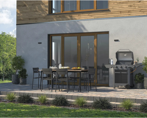 Uteplats med trädgårdsbord, stolar och grill framför ett bostadshus.