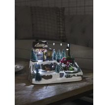 Belyst juldekoration med hus, figurer och granar på en snöig yta.