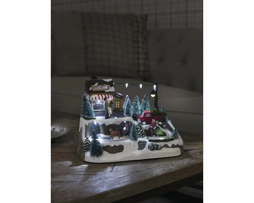 Belyst juldekoration med hus, figurer och granar på en snöig yta.