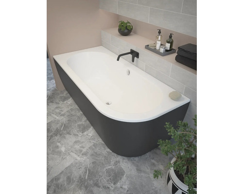 Fristående badkar i ett badrum med kakelvägg och växt