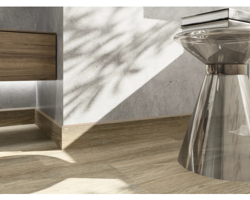 Detaljbild av en interiör med trägolv, golvsockel och ett sidobord