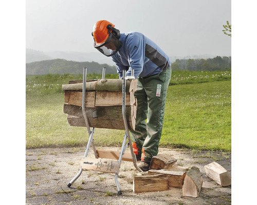 En person använder en vedkapningsbock för att såga trädstammar i en utomhusmiljö.
