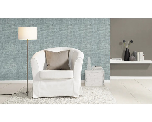 Vardagsrum med ljusblå textilväggbeklädnad, vit fåtölj och golvlampa.