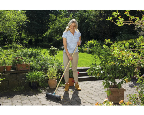 Kvinna sopar en uteplats i en trädgård med en kvast.