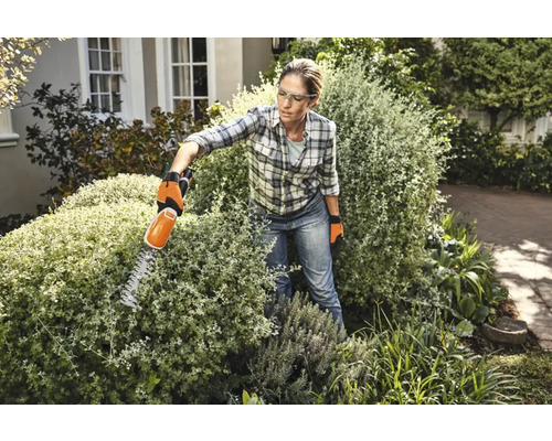 Kvinna klipper häck med en häcksax i trädgården.