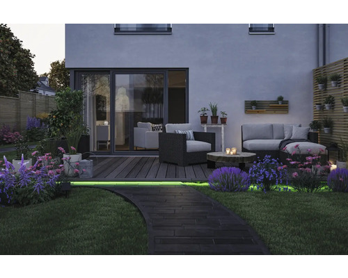 Atmosfärisk trädgård med loungemöbler, träterrass och upplyst stig