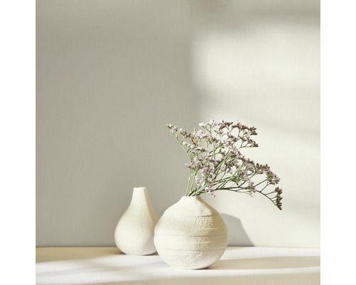 Två vita vaser, en med torkade blommor, på en ljus bakgrund.