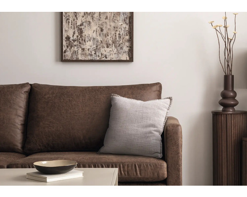 Vardagsrumsscen med brun lädersoffa, prydnadskudde, bord, dekoration och konstverk