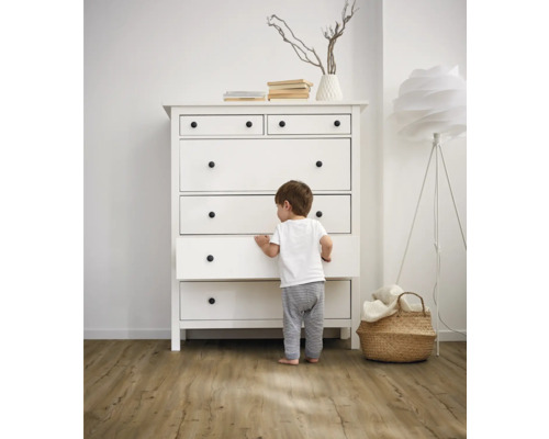 Ett barn står framför en vit byrå med lådor och runda handtag i ett ljust rum.