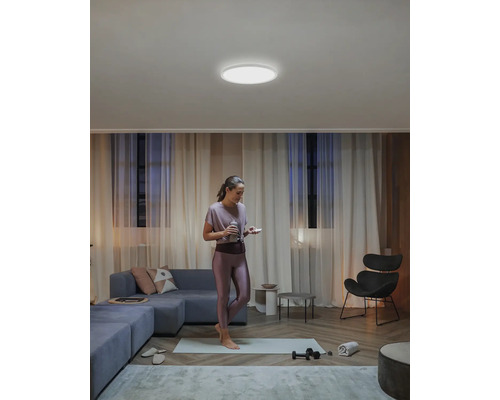 En kvinna står på en yogamatta i ett vardagsrum med en rund taklampa.