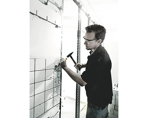 En man använder en hammare och mejsel för att ta bort kakel från en vägg.