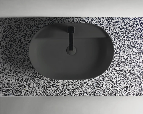 Ovanifrån en oval, svart tvättställsskål med armatur på en bänkskiva med terrazzomönster.