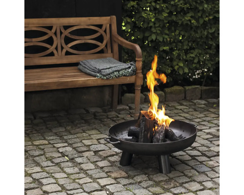 Eldstad med trä och lågor i trädgården, bredvid en träbänk med filt