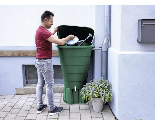 Man fyller en regntunna med vattenkanna och hink.