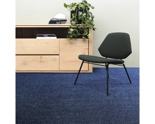 Vardagsrum med byrå, växt, spegel, bok och stol på blå heltäckningsmatta.