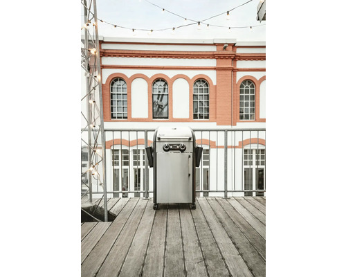 Gasolgrill i rostfritt stål på en terrass framför en byggnad