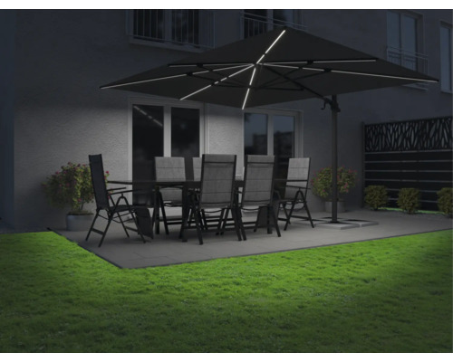 Trädgårdsmöbler under ett upplyst parasoll på en terrass med gräsmatta