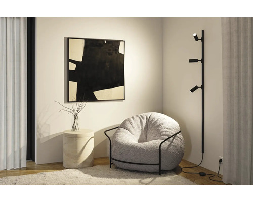 Inredningshörna med fåtölj, golvlampa, sidobord och konstverk