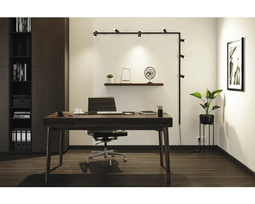 Modernt arbetsrum med skrivbord, kontorsstol, hyllsystem och vägglampa.