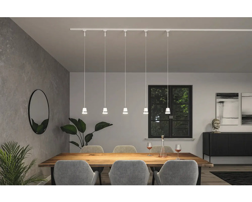 Matsal med matbord, stolar, krukväxter, spegel, skänk, dekoration och en vit skenspotlight med fem hänglampor.