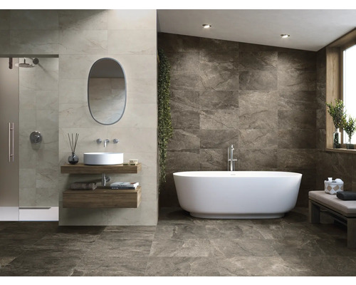 Badrum med dusch, handfat, spegel och fristående badkar mot en kakelvägg.