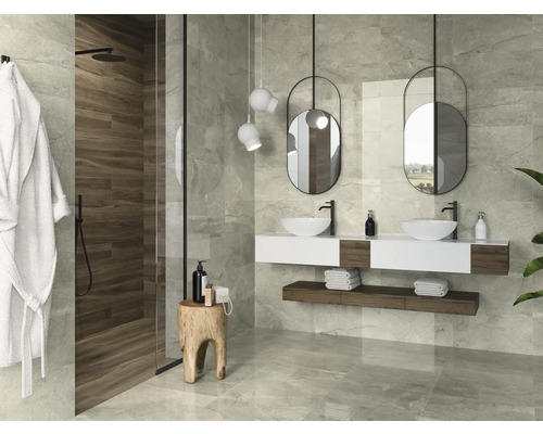 Ljust badrum med dusch, dubbla handfat, hängande speglar och gråa plattor.