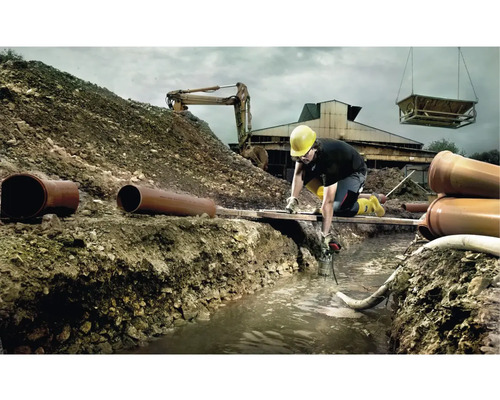 Byggarbetsplats med byggnadsarbetare, grävmaskin och rör under grävningsarbetet