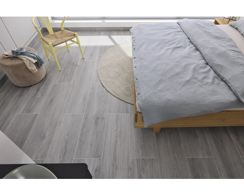 Sovrum med säng, stol, pall, matta och grå golvplattor med träutseende