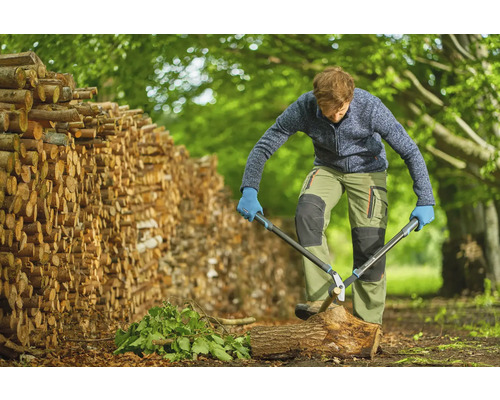 Man hugger ved med en grensax bredvid en vedstapel.