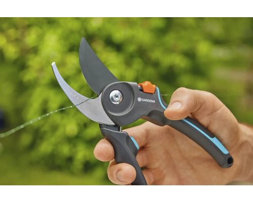 En hand håller en Gardena trädgårdssax som klipper av en tunn gren.