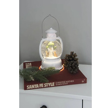 Dekorativ lykta med snöglob, ängel och julgran på ett nattduksbord