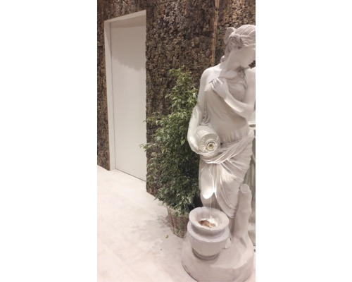 Dekorativ scen med en kvinnlig staty, krukväxt och en vägg med trädbark