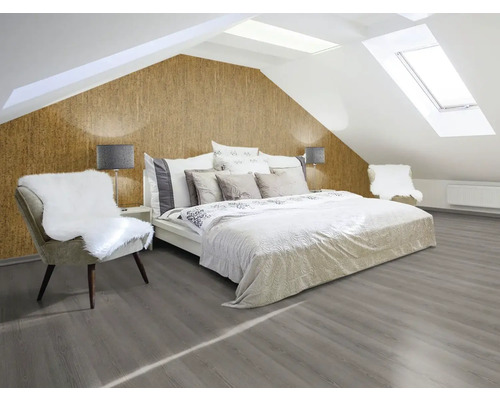 Ljust sovrum med sluttande väggar, korktapet, säng, stol och grått trägolv