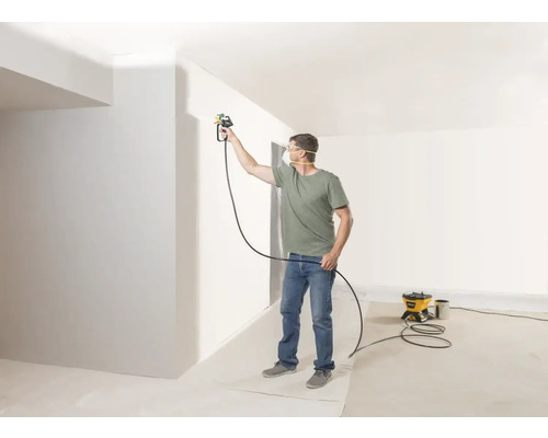 Man målar vägg med färgspraysystem i ljust rum