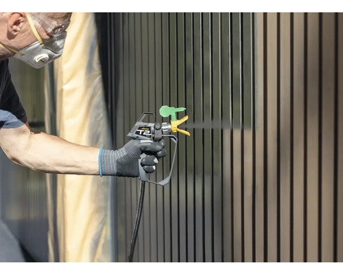 Person lackerar staket med färgspruta