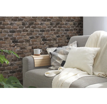 Dekorativt vardagsrum med grå soffa, kuddar, pläd och vägg i tegelstenslook.