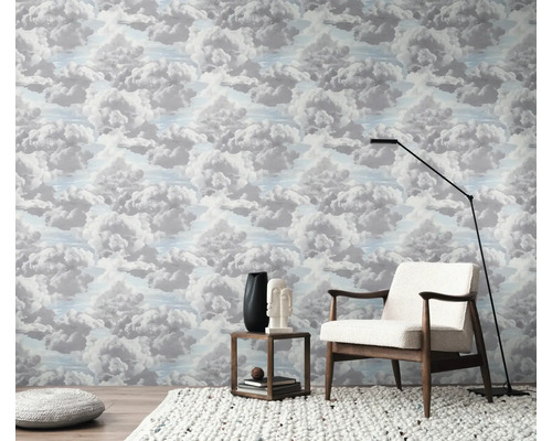 Ett rum med tapet med molnmönster, en fåtölj, en golvlampa och ett sidobord.
