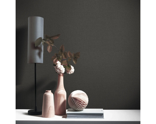 Närbild av en svart textiltapet med dekorativa element som en lampa, vas och bok