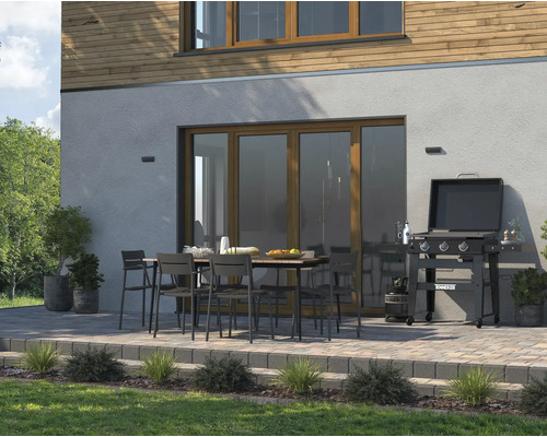 Terrass med grill, trädgårdsbord och trädgårdsstolar framför husvägg