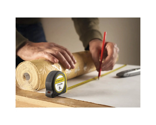 En person mäter en tapetrulle med ett måttband och markerar den med en penna.