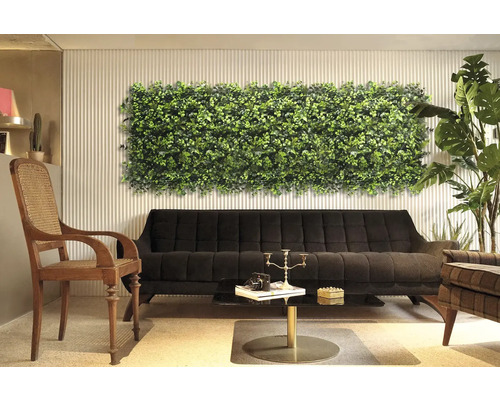 Dekorativ interiör med växtväggspanel ovanför en svart soffa.