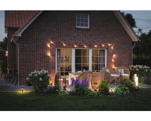 Terrass med trädgårdsmöbler, upplyst med en ljusslinga och trädgårdslampor, på kvällen