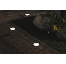 Miljöbild med infällda markspotlights på en träaltan, bredvid stenar och växter.