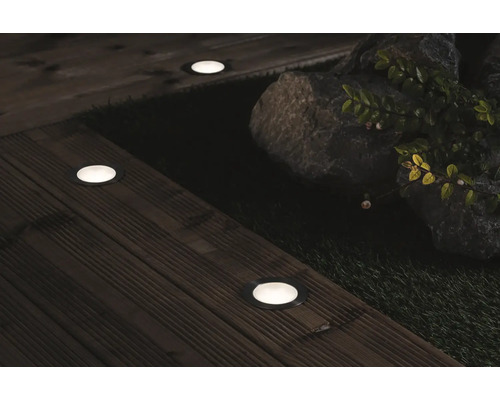 Miljöbild med infällda markspotlights på en träaltan, bredvid stenar och växter.