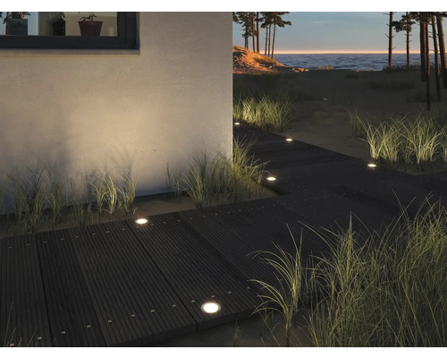 Scen med en trägång belyst av infällda lampor som leder till en strand.