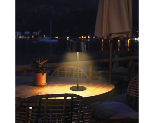 Utomhusbild av en bordslampa på ett träbord utomhus på natten.