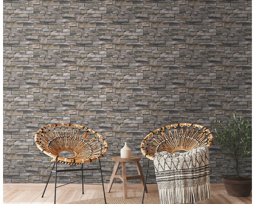 Två rottingfåtöljer framför en vägg med tapet i stenimitation i ett ljust rum.