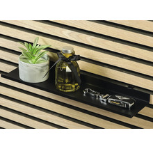 Dekorativ krukväxt, doftflaska och nycklar på en svart vägghylla framför en trävägg