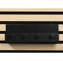 Svart kroklist med fyra krokar framför en träpanelvägg