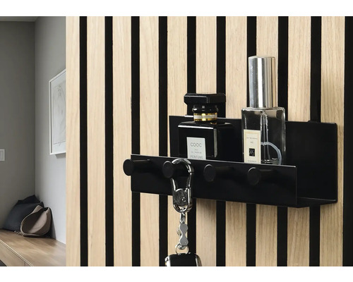 Svart nyckelhållare med krokar och två parfymflaskor på en vägg med träpanel